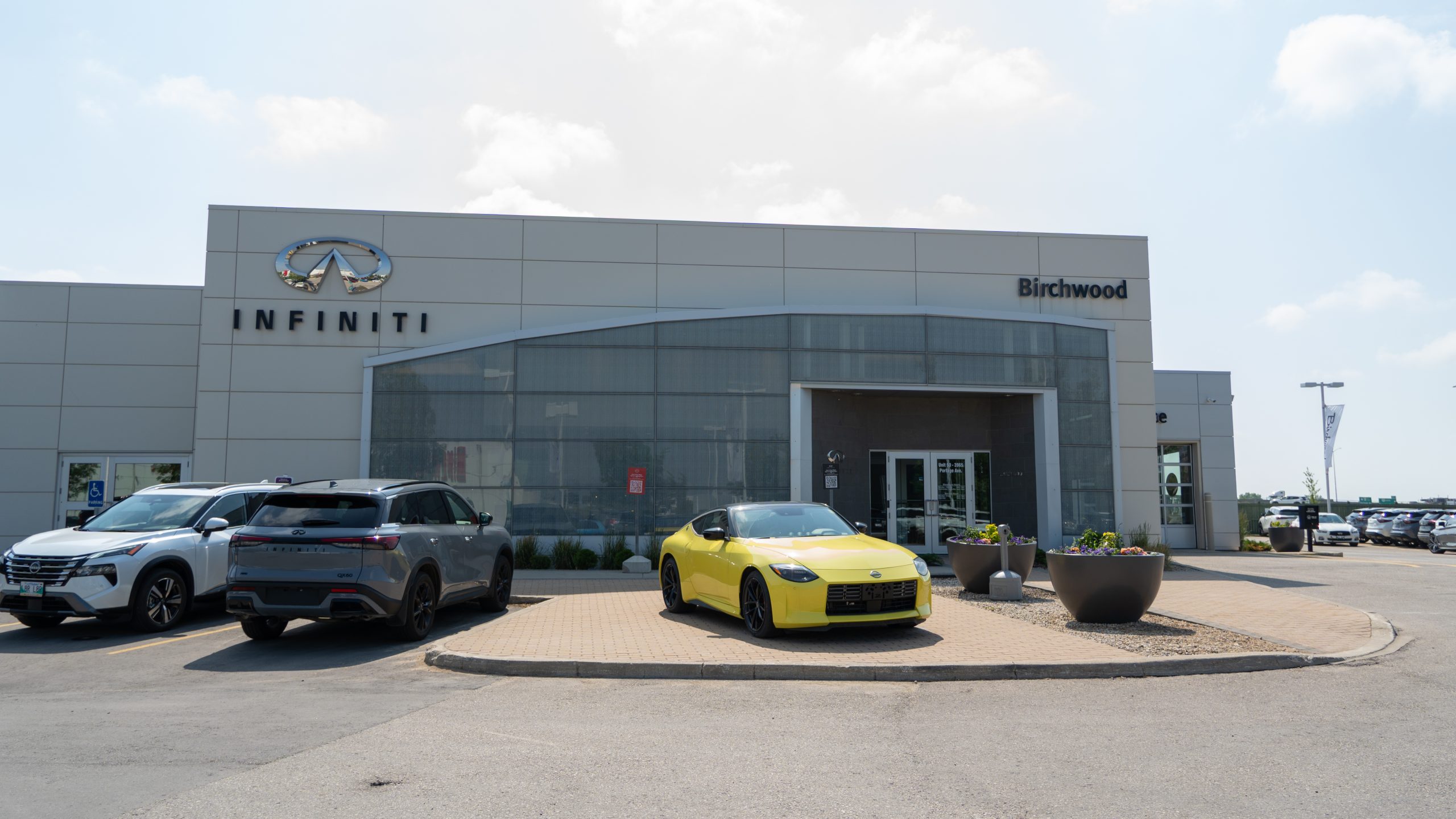 Exterior of Birchwood INFINITI dealership with a clean modern facade, INFINITI and Birchwood signage, and a bright yellow Nissan sports car displayed near the entrance.